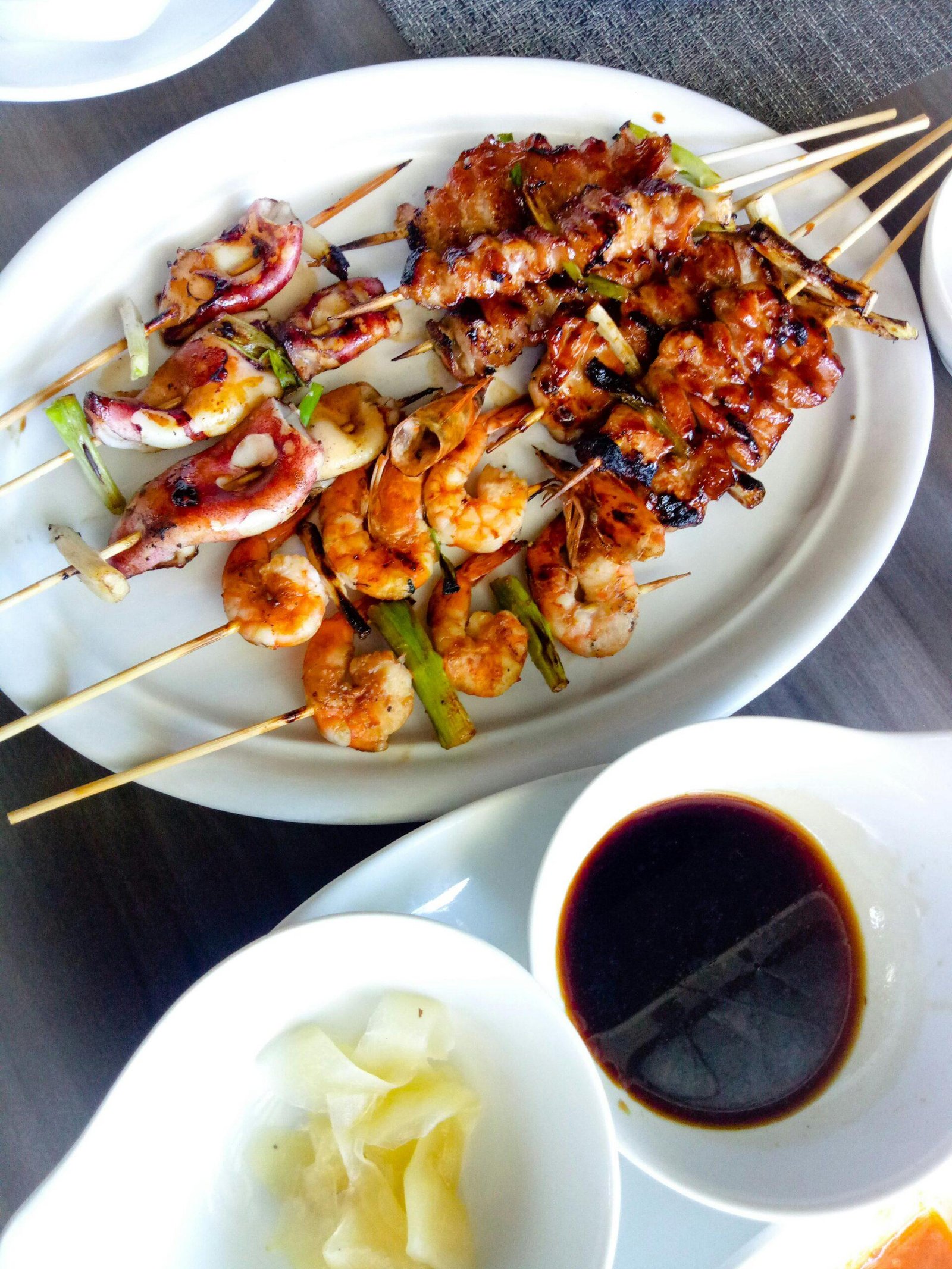 Delicious grilled skewers including shrimp and squid served with sauce on a white plate.